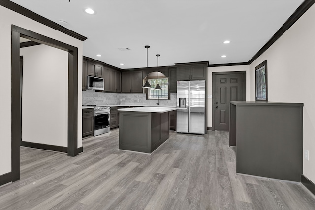 kitchen with pendant lighting, a kitchen island, appliances with stainless steel finishes, crown molding, and light hardwood / wood-style floors