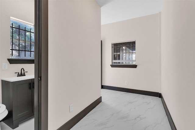hallway with marble finish floor, baseboards, and a sink