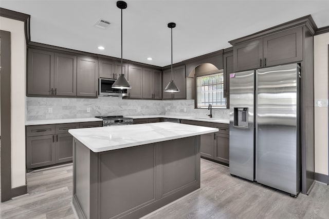 kitchen with appliances with stainless steel finishes, a kitchen island, pendant lighting, and light hardwood / wood-style flooring