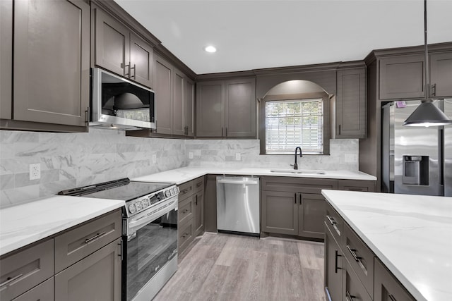 kitchen with decorative backsplash, sink, light hardwood / wood-style floors, hanging light fixtures, and appliances with stainless steel finishes