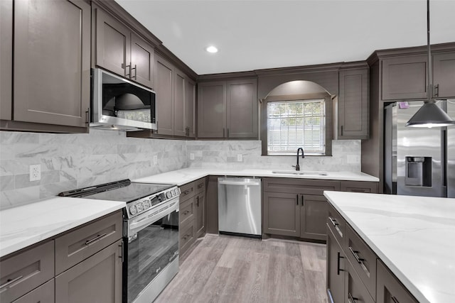 kitchen with a sink, light wood-style floors, light stone countertops, tasteful backsplash, and appliances with stainless steel finishes