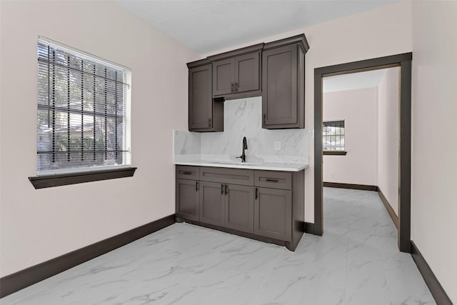 kitchen featuring baseboards, light countertops, marble finish floor, and a sink
