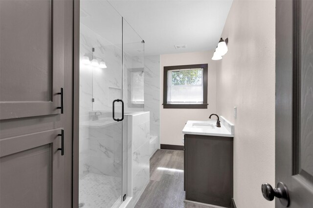 bathroom with wood finished floors, a marble finish shower, vanity, baseboards, and visible vents