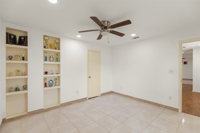 tiled spare room with ceiling fan and built in shelves