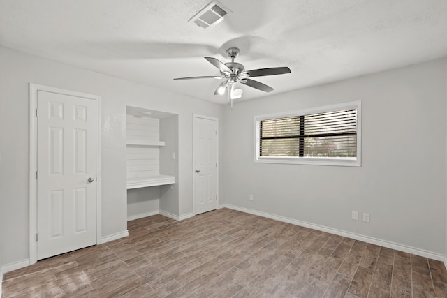 unfurnished bedroom featuring built in desk, a textured ceiling, light hardwood / wood-style floors, and ceiling fan