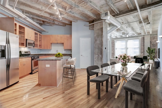 kitchen with appliances with stainless steel finishes, a center island, light wood-type flooring, and a high ceiling