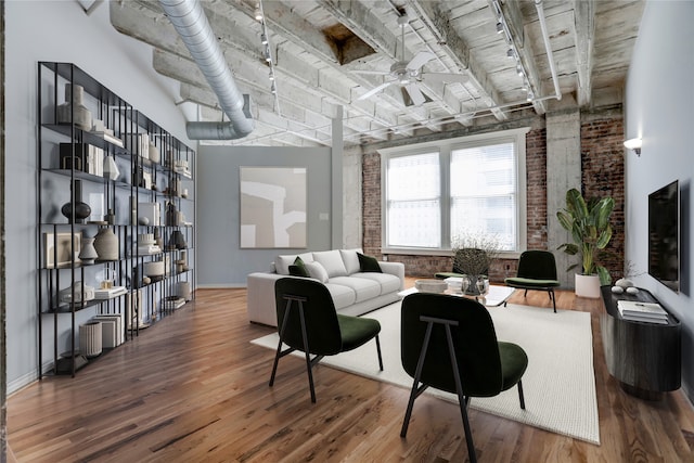 living area with brick wall, track lighting, ceiling fan, and wood finished floors