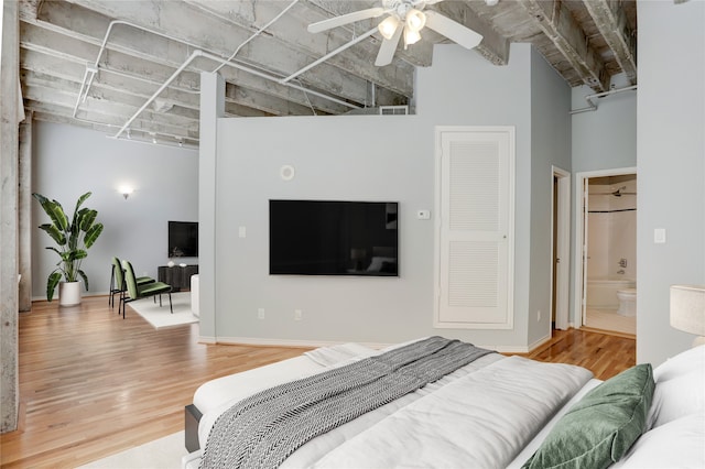 bedroom with ceiling fan, wood-type flooring, a high ceiling, and connected bathroom