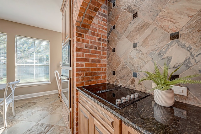 kitchen featuring black electric stovetop, oven, a healthy amount of sunlight, and dark stone countertops