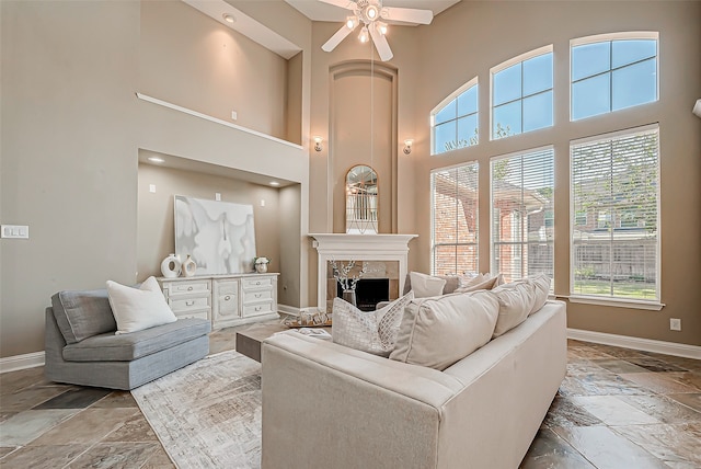 living room with ceiling fan, a fireplace, and a towering ceiling