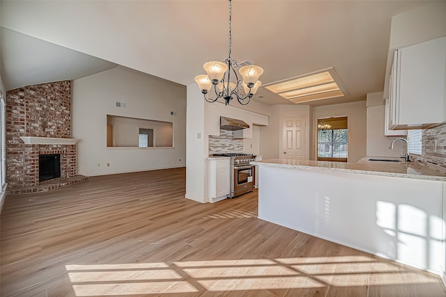 kitchen with sink, hanging light fixtures, white cabinetry, high end stainless steel range, and light hardwood / wood-style flooring