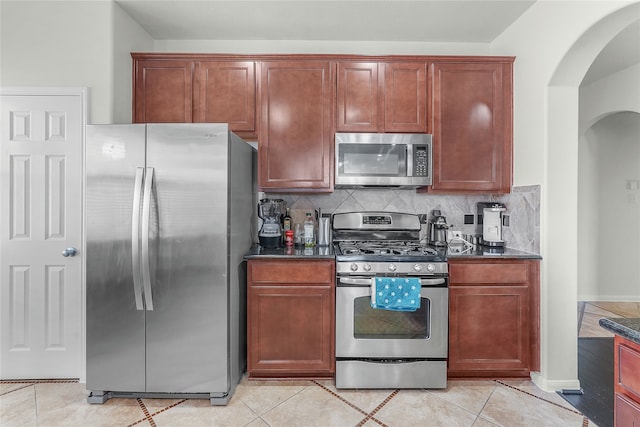 kitchen featuring light tile patterned flooring, stainless steel appliances, backsplash, and dark stone counters