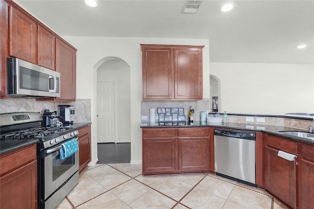 kitchen with stainless steel appliances, tasteful backsplash, dark stone countertops, sink, and light tile patterned floors