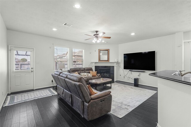 living room with ceiling fan, a tiled fireplace, and dark hardwood / wood-style floors