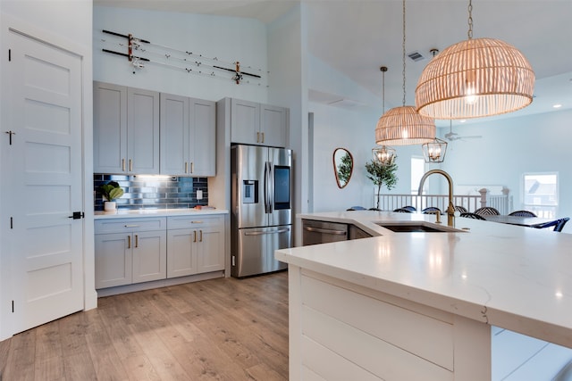 kitchen featuring appliances with stainless steel finishes, light stone countertops, light hardwood / wood-style flooring, pendant lighting, and sink