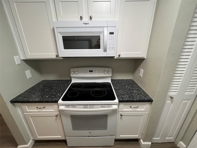 kitchen with white cabinets, dark stone counters, and white appliances