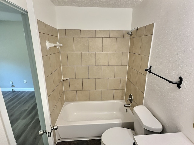 bathroom featuring a textured ceiling, toilet, and tiled shower / bath