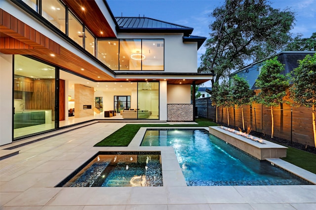 pool at dusk featuring pool water feature, a patio area, and a hot tub