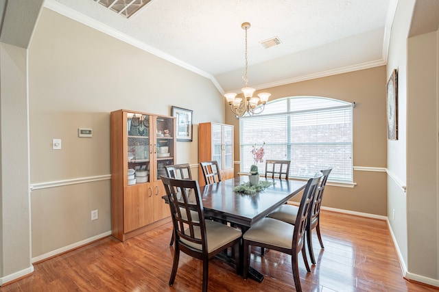 dining space featuring lofted ceiling, wood-type flooring, a textured ceiling, an inviting chandelier, and crown molding