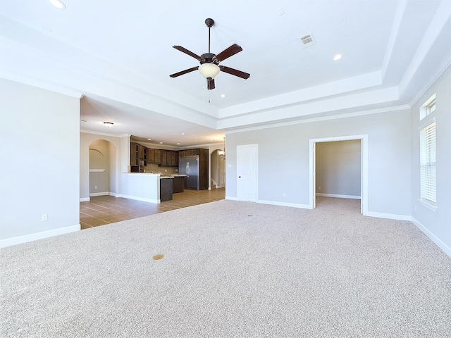 unfurnished living room with ornamental molding, ceiling fan, light colored carpet, and a raised ceiling