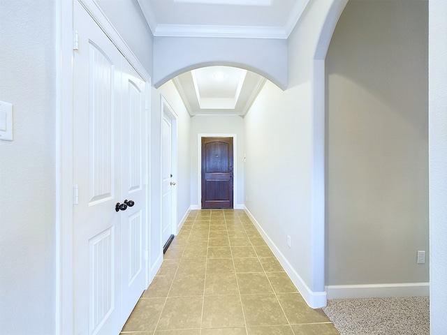 hallway with crown molding, light tile patterned flooring, and a raised ceiling