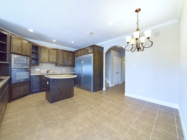 kitchen with built in appliances, hanging light fixtures, dark brown cabinets, ornamental molding, and a center island