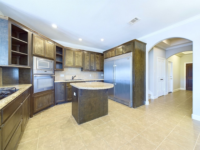 kitchen featuring built in appliances, backsplash, ornamental molding, a center island, and dark brown cabinetry