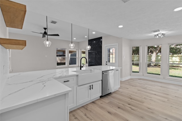 kitchen featuring pendant lighting, white cabinets, sink, stainless steel dishwasher, and light stone countertops