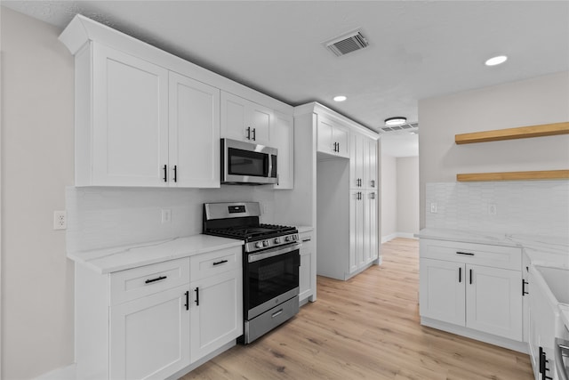 kitchen featuring light hardwood / wood-style floors, white cabinetry, light stone countertops, and appliances with stainless steel finishes