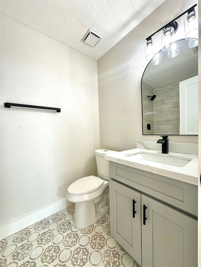 bathroom with tiled shower, vanity, a textured ceiling, and toilet