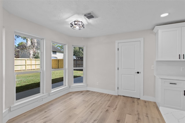 unfurnished dining area with light wood-type flooring and a textured ceiling