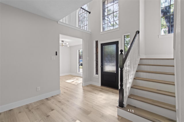 entrance foyer with a wealth of natural light, light wood-type flooring, a high ceiling, and an inviting chandelier