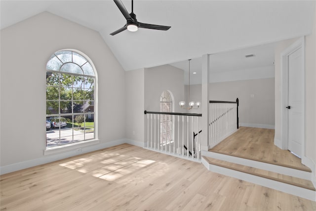 spare room featuring a wealth of natural light, lofted ceiling, ceiling fan with notable chandelier, and light wood-type flooring