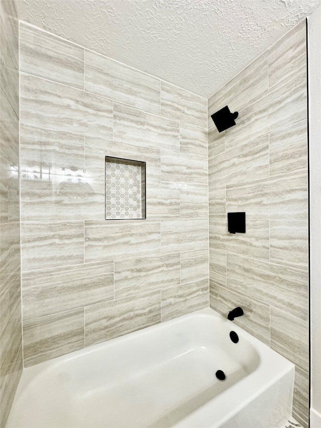 bathroom featuring a textured ceiling and tiled shower / bath