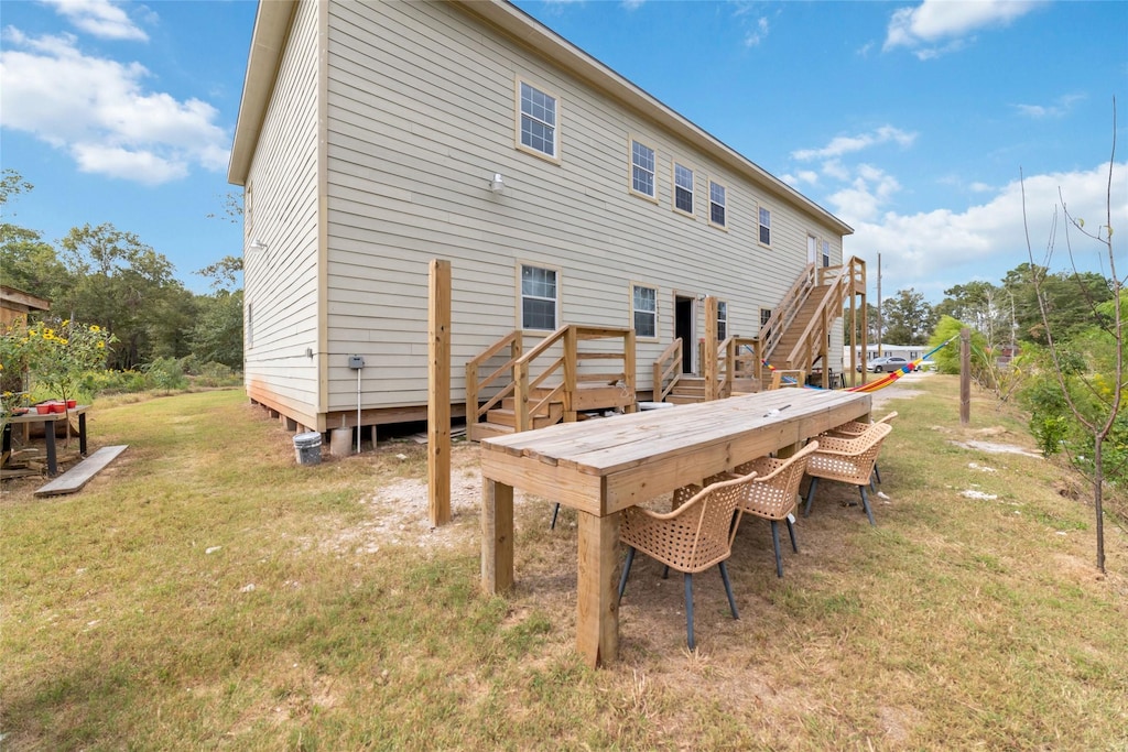 back of property featuring stairway, a deck, and a lawn