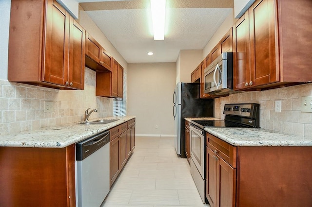 kitchen featuring appliances with stainless steel finishes, decorative backsplash, sink, and light stone counters