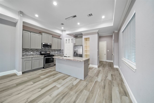 kitchen featuring gray cabinets, backsplash, a center island with sink, hanging light fixtures, and appliances with stainless steel finishes