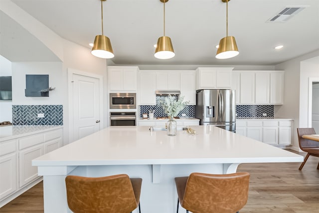 kitchen featuring white cabinetry, tasteful backsplash, stainless steel appliances, and an island with sink