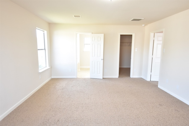 unfurnished bedroom featuring a spacious closet, light colored carpet, and a closet