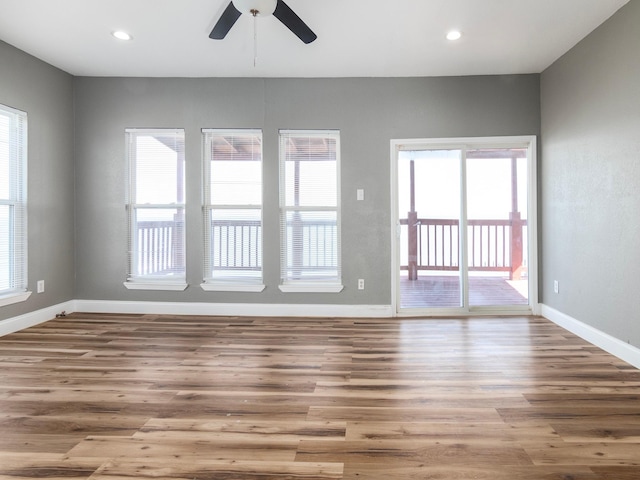 spare room with wood finished floors, baseboards, ceiling fan, and a healthy amount of sunlight