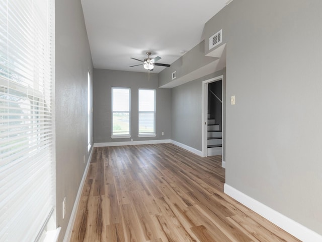 empty room featuring baseboards, visible vents, a ceiling fan, wood finished floors, and stairs