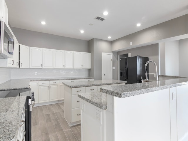 kitchen with light stone countertops, white cabinetry, stainless steel appliances, light hardwood / wood-style flooring, and a kitchen island with sink