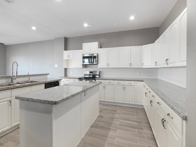 kitchen with white cabinetry, stainless steel appliances, light stone counters, and a kitchen island