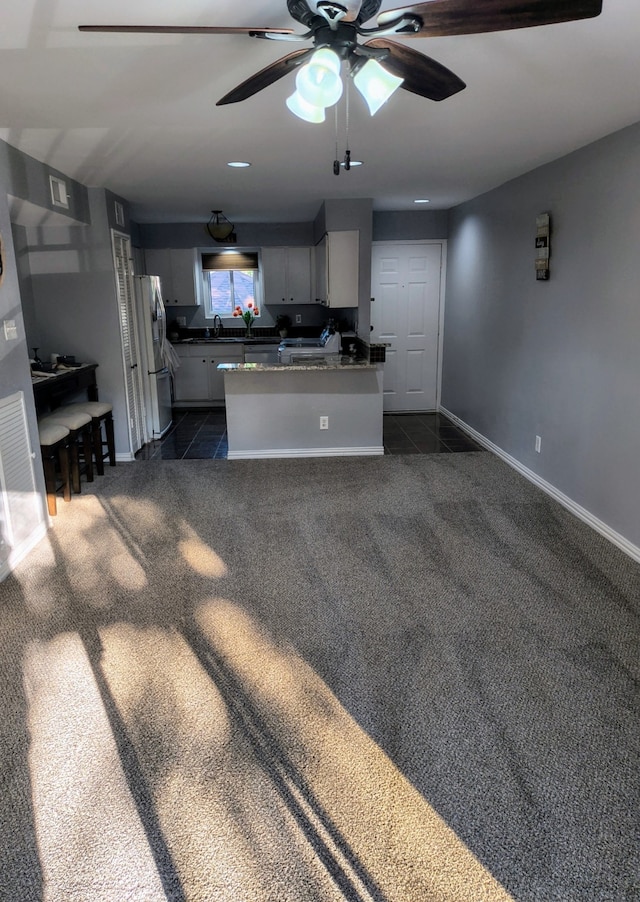 kitchen with ceiling fan, kitchen peninsula, white cabinetry, dark colored carpet, and white fridge