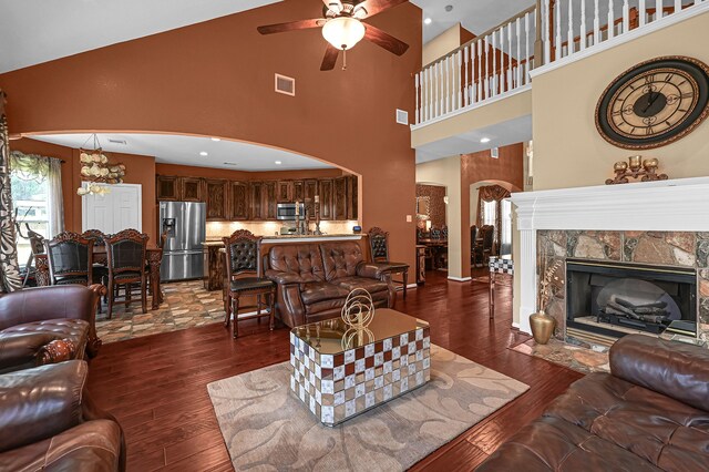 living room with ceiling fan with notable chandelier, dark hardwood / wood-style flooring, and a high ceiling