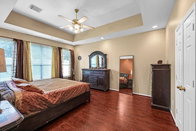 bedroom with ceiling fan, a closet, dark hardwood / wood-style floors, and a raised ceiling