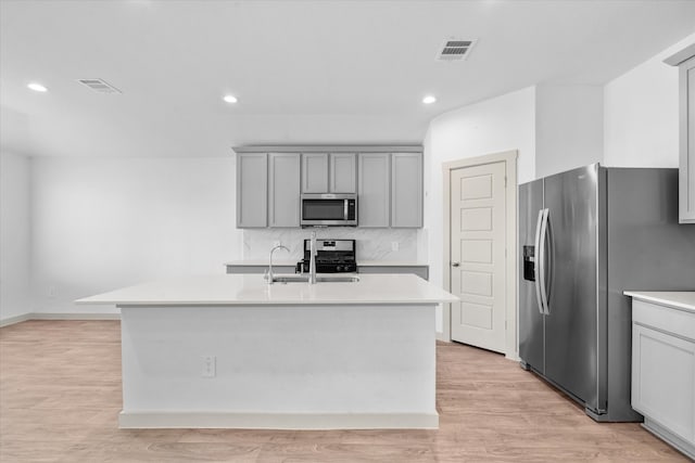 kitchen featuring sink, appliances with stainless steel finishes, light hardwood / wood-style flooring, and an island with sink