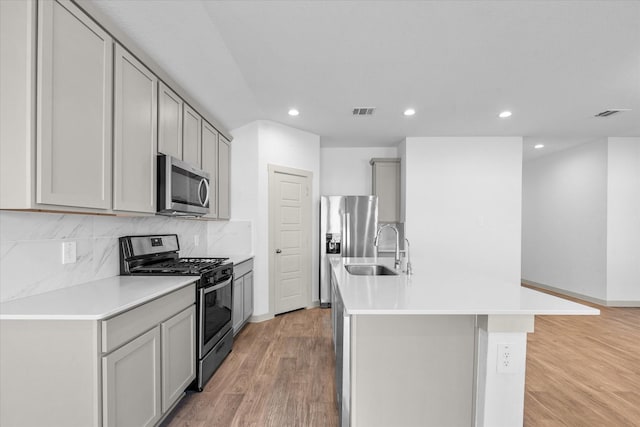 kitchen with an island with sink, visible vents, gray cabinets, a sink, and stainless steel appliances