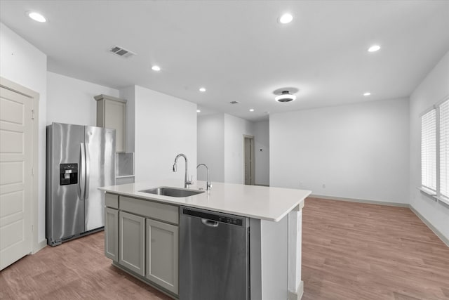 kitchen with gray cabinetry, sink, light hardwood / wood-style floors, stainless steel appliances, and a kitchen island with sink