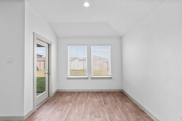 spare room featuring light wood-style flooring, baseboards, and lofted ceiling